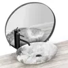 A marble basin with a black faucet is shown on a wooden countertop, with a round mirror reflecting the scene. Náhled obrázku produktu