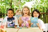 Four children are sitting at a table outdoors, holding up sticker albums. Produktbild-Vorschau