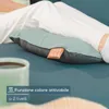 A person's legs are resting on a teal surface, with a massage pillow placed underneath their legs. A cup is visible in the foreground. Produktbild-Vorschau