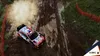 A rally car kicking up dust on a dirt track, with trees and orange safety netting on the sides. Produktbild-Vorschau