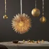 A festive arrangement of Christmas decorations, including a large paper star lantern and several golden baubles, set against a dark background. Podgląd zdjęcia produktu
