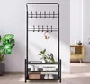A black metal coat rack with shelves is shown in a room with a large plant and a wooden cabinet in the background. Produktbild-Vorschau