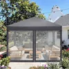 A grey pop-up gazebo with mesh sides, set up on a patio with outdoor furniture inside. It is surrounded by a garden with flowers and trees, and string lights are visible overhead. Podgląd zdjęcia produktu