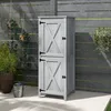 A light gray wooden garden cabinet with double doors and black hardware stands on a patio next to a fence and plants. Náhľad obrázku produktu