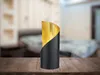 A table lamp with a black base and a gold interior is placed on a wooden table in front of a blurred bedroom background. Voir les images du produit