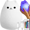 A white cat-shaped LED night light is shown with a remote control and charging cables. Another cat-shaped light is being held by hands and is illuminated with purple and blue light. Produktbild-Vorschau