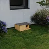 A wooden cat house is placed on a green lawn next to a white wall and some bushes. Náhled obrázku produktu