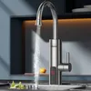 A modern kitchen faucet with a digital temperature display is shown in use, with water flowing into a sink. The background features a dark blue cabinet and a warm orange light. Podgląd zdjęcia produktu