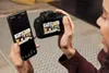 A person is holding a camera and a smartphone, seemingly transferring photos. Voir les images du produit