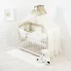 A baby crib set with bedding and accessories, including a teddy bear, displayed in a room setting. Produktbild-Vorschau