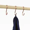 Three rose gold S-hooks are hanging from a wooden rod. One hook has a dark blue fabric item hanging from it. Produktbild-Vorschau