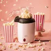 A popcorn machine is shown in action, with popcorn popping out and filling striped containers. Podgląd zdjęcia produktu