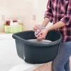 A person is washing a colorful cloth in a dark gray basin placed on the edge of a bathtub. Produktbild-Vorschau