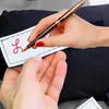 A close-up shot of a hand writing on a white label with a pen, with another hand underneath. Voir les images du produit
