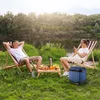 A couple enjoying a picnic by a river, with a cooler box and food on a table. Náhled obrázku produktu