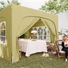 A woman sits in a chair outside a green pop-up gazebo, holding a mug. A table is set inside the gazebo with a tablecloth, a lamp, and some fruit. Podgląd zdjęcia produktu