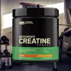 A tub of creatine powder is placed in a gym setting. Produktbild-Vorschau