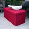 A person's feet in white socks rest on a red storage ottoman in a living room setting. Náhled obrázku produktu