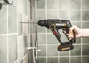 A hand holding a cordless hammer drill against a tiled wall. Produktbild-Vorschau