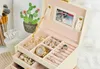An open jewelry box filled with various accessories, including necklaces, earrings, rings, and a watch, next to makeup brushes and a small framed picture of a cactus. Náhľad obrázku produktu