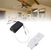 A black fan receiver and a white remote control are shown in front of a blurred image of a living room with a ceiling fan and windows. Podgląd zdjęcia produktu