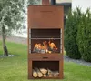 A rusty metal grill with a fire burning inside, set up in a garden with grass and trees. Voir les images du produit