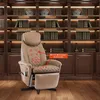 A beige massage chair is positioned in front of a large, dark wood bookshelf filled with books, set in a room with wooden flooring. Produktbild-Vorschau