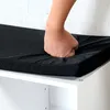 A hand is pressing down on a black cushion on top of a white cabinet. Produktbild-Vorschau