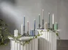 A collection of LED candles in various colors and sizes arranged on white pedestals, with ivy vines draped around them. Podgląd zdjęcia produktu