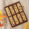 A silicone mold filled with granola bars on a wooden surface, with some dried fruit and nuts scattered around. Anteprima dell’immagine prodotto