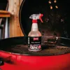 A bottle of grill cleaner is placed on the grill rack of an open red grill. Produktbild-Vorschau