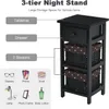 A black three-tier nightstand with a drawer and two baskets, shown with labels indicating its features and examples of items that can be stored. Náhled obrázku produktu