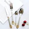 A set of cutlery is laid out on a white surface with a book in the background and two cherries in the foreground. Produktbild-Vorschau