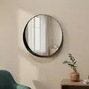 A round mirror hangs on a light beige wall above a wooden side table with a vase and a plant. Produktbild-Vorschau