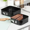 Two square springform pans are shown on a kitchen counter. One pan is empty, and the other contains a slice of chocolate cake. Anteprima dell’immagine prodotto