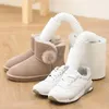 A boot dryer with two nozzles is shown drying a pair of beige boots and a pair of white sneakers. Produktbild-Vorschau