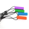 Four colorful teething toys shaped like building blocks are arranged diagonally on a white background, attached to black strings. Produktbild-Vorschau