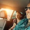 A father and son are in a car, with a tablet mounted on the back of the father's headrest for the son to watch. Anteprima dell’immagine prodotto