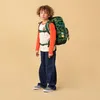 A young boy wearing a backpack stands against a plain background. Produktbild-Vorschau