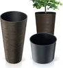 Three plant pots are displayed against a white background. One tall, textured brown pot is on the left. Another similar brown pot, containing a small green plant, is in the background. A smaller, plain black pot is in the foreground on the right. Anteprima dell’immagine prodotto
