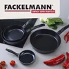 A collection of black frying pans of various sizes, along with fresh vegetables and chili peppers, arranged on a countertop. Produktbild-Vorschau