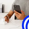 A person is holding a black smartphone while it is charging from a white power adapter and cable. Anteprima dell’immagine prodotto