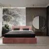 A bedroom with a pink upholstered bed, black bedding, and a large round mirror. Produktbild-Vorschau