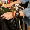 A person is browsing through clothes on hangers, wearing a watch and a bracelet. Produktbild-Vorschau