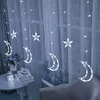 A string of moon and star-shaped fairy lights hanging in front of a sheer curtain, with a small table with books and a jar of lights in the foreground. Náhľad obrázku produktu