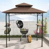 A grill pavilion set up on a patio with a grill, accessories, and a scenic background of water and mountains. Produktbild-Vorschau