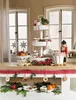 A festive Christmas display on a wooden table, featuring a tiered stand with treats, bowls of fruit and nuts, and decorative elements like a nutcracker and pine branches. Produktbild-Vorschau