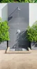 An outdoor shower area with a tiled wall, shower head, and drain. Produktbild-Vorschau