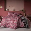 A bedroom scene with a bed dressed in a red paisley patterned duvet and pillows, a grey throw blanket draped over the bed, and decorative items on shelves in the background. Produktbild-Vorschau