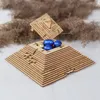 A wooden pyramid-shaped puzzle box filled with foil-wrapped chocolate eggs, set against a background of dried reeds. Podgląd zdjęcia produktu